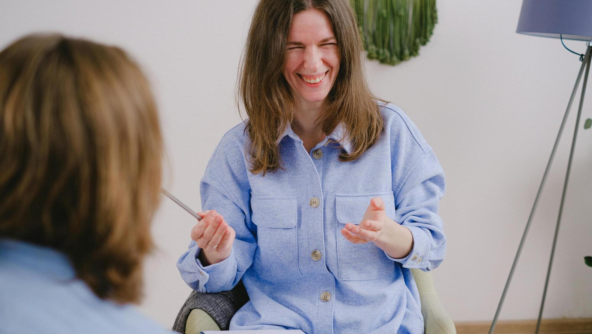 Kvinna med anteckningsblock och penna som skrattar. Symbol för att det ska vara roligt att arbeta med kommunikationen på försäkringsbolag.